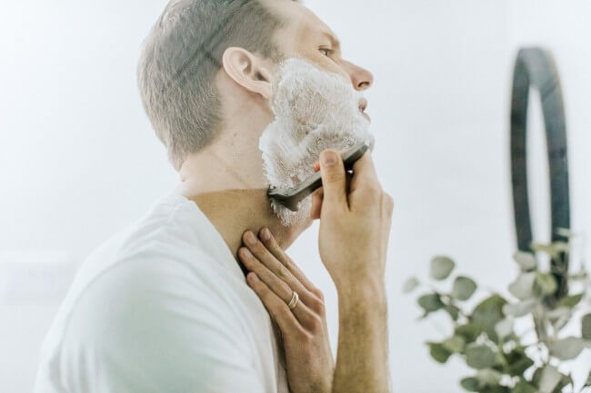 a man shaving beard in front of mirror in bathroom